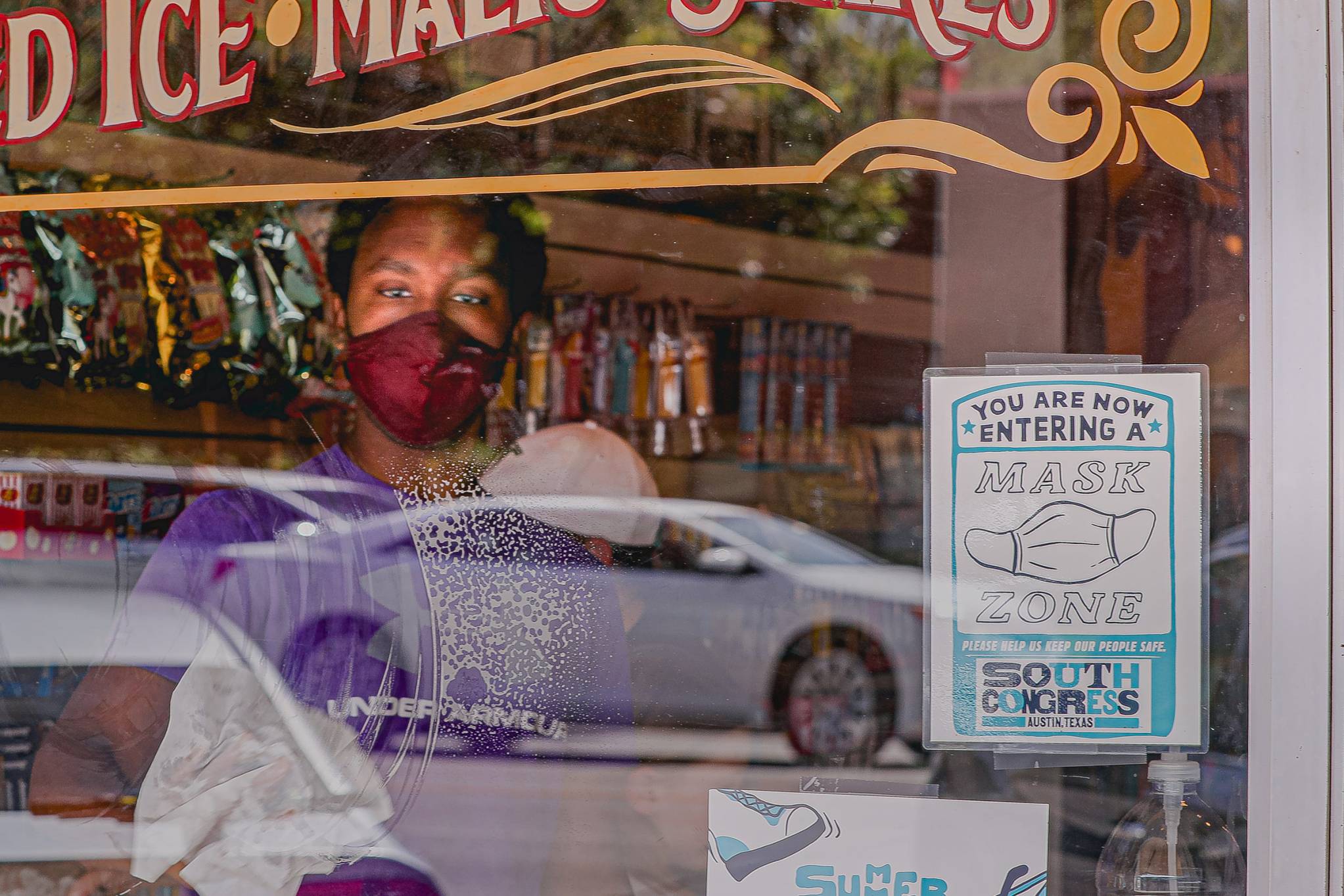 A store employee wearing a mask cleans a window with a sign requesting customers put on masks at a shop on Austin's South Congress Avenue on Sept. 30.
